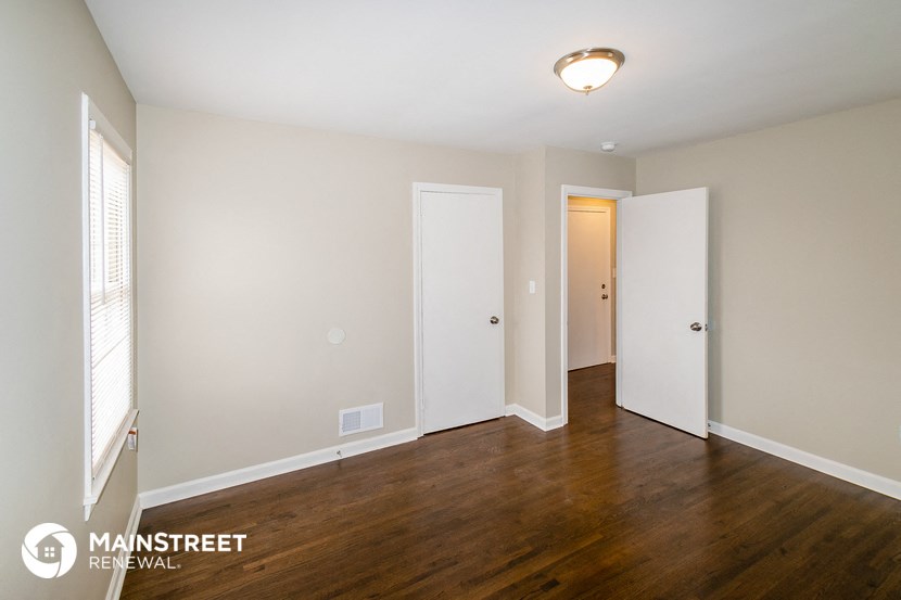 a living room with wood flooring and white walls and a door to a hallway