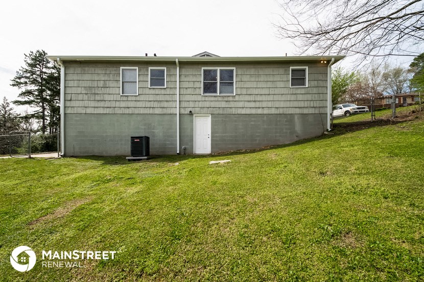 the front of a small gray house with a green lawn