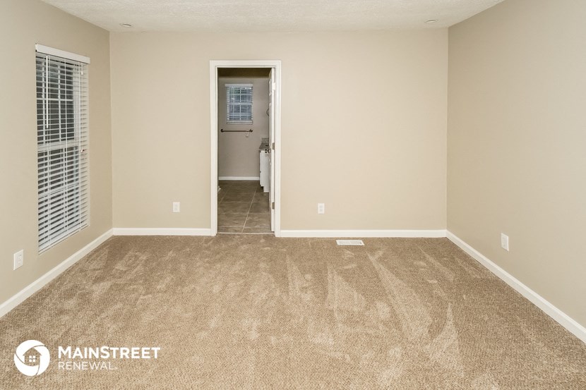 an empty living room with carpet and a door to a bathroom