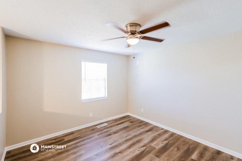 the spacious living room with hardwood flooring and a ceiling fan