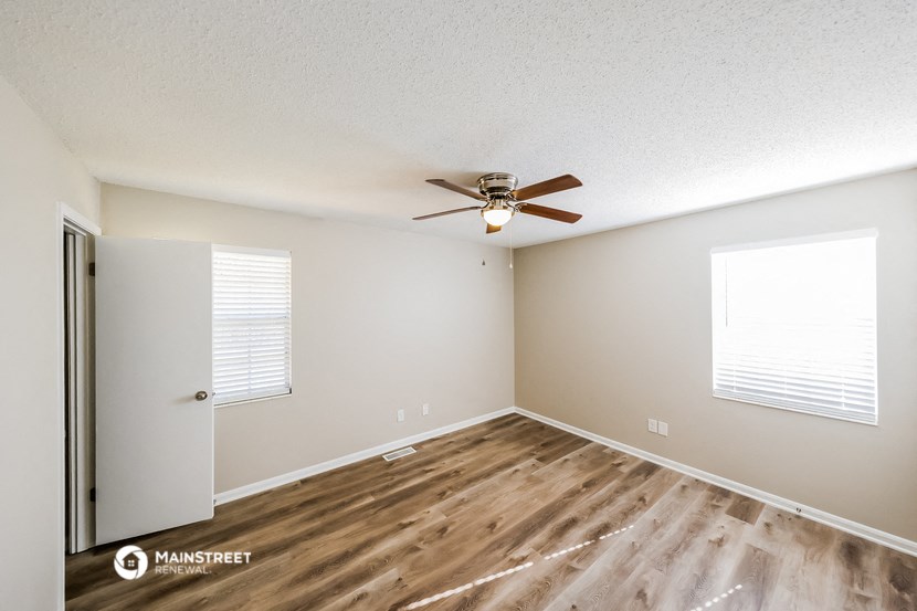 the spacious living room with hardwood flooring and a ceiling fan
