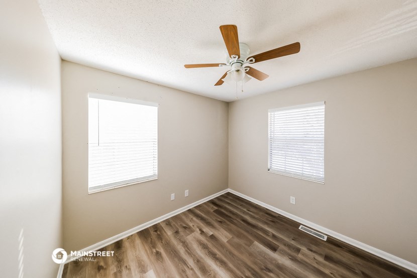 an empty room with a ceiling fan and two windows
