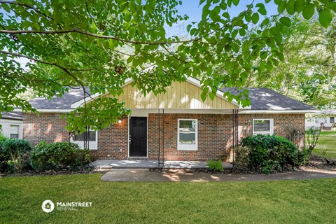 the front of a brick house with a yard and a tree