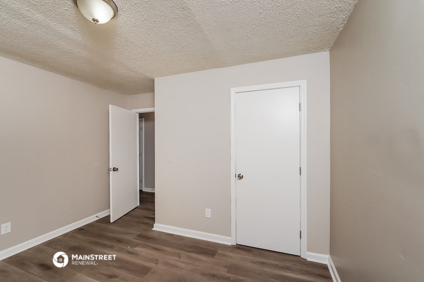 the living room of an apartment with white walls and wood flooring