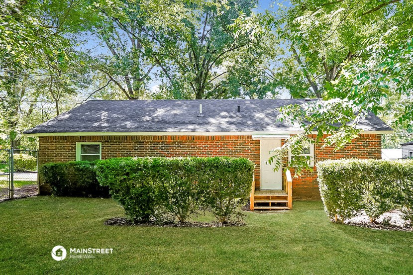 a small brick house with a porch and a lawn