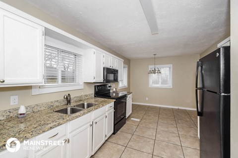 a kitchen with white cabinets and granite counter tops and a black refrigerator