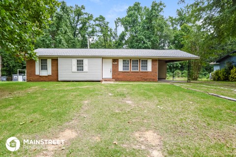 a small brick house with a grassy yard and trees