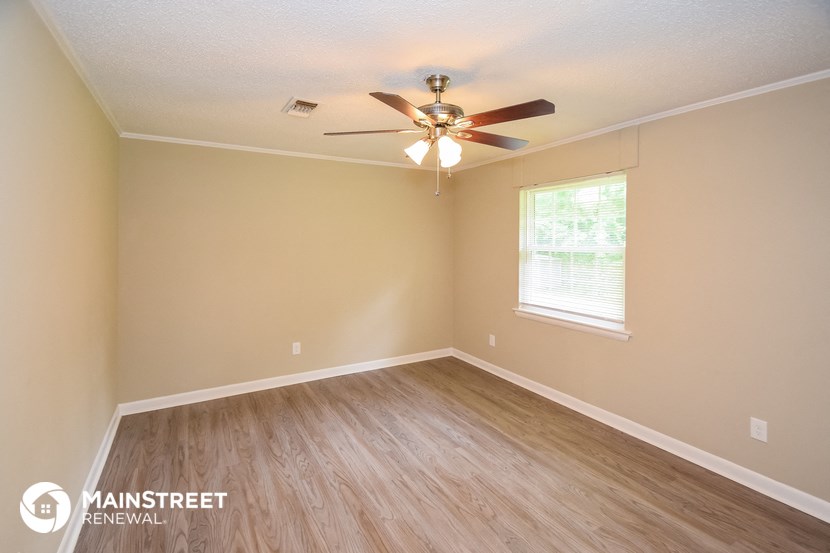 the spacious bedroom with hardwood flooring and a ceiling fan