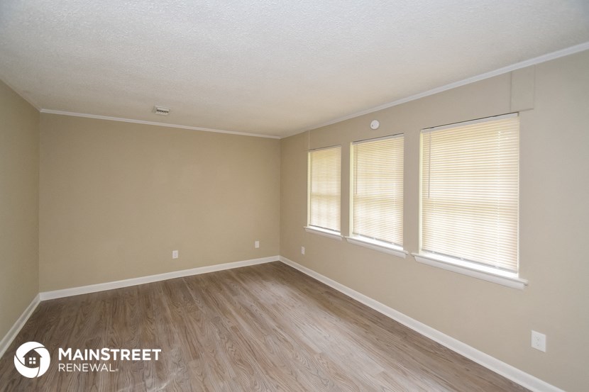 the spacious living room with wood flooring and three windows