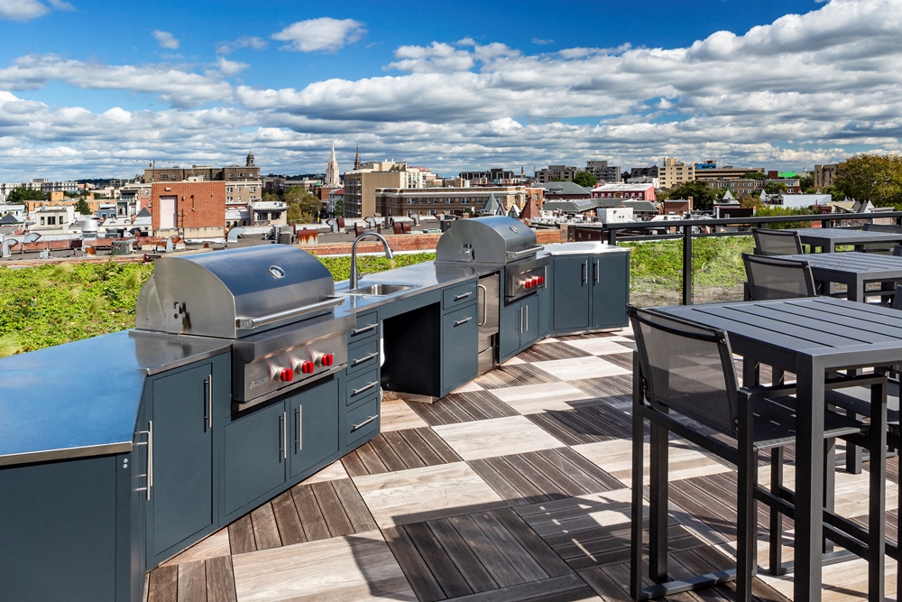a rooftop barbecue area with tables and bbqs and a city in the background