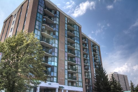 A tall building with many windows and balconies is surrounded by trees.