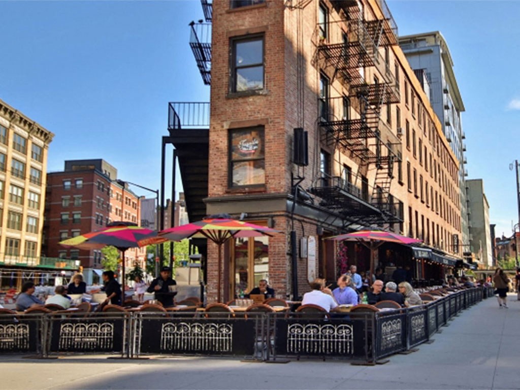 people sitting at restaurants on the side of a city street