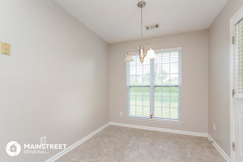 a spacious living room with a large window and beige carpet