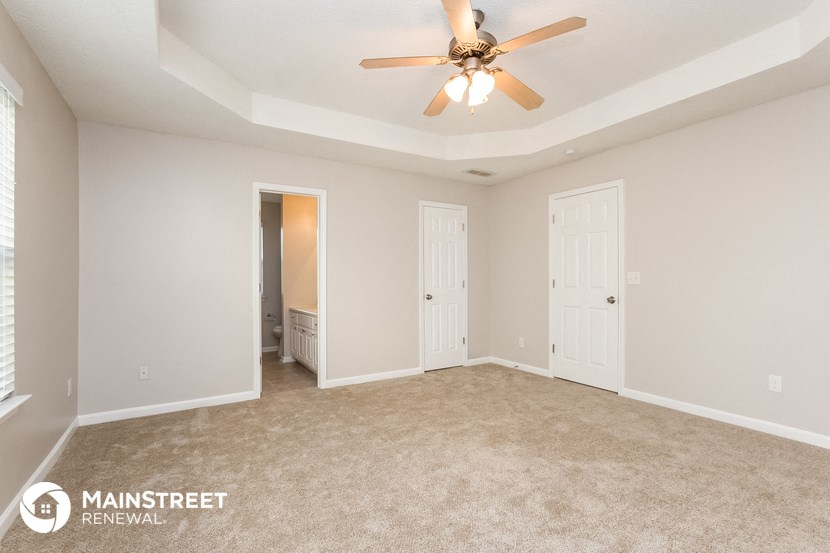 the spacious living room with ceiling fan and carpeting