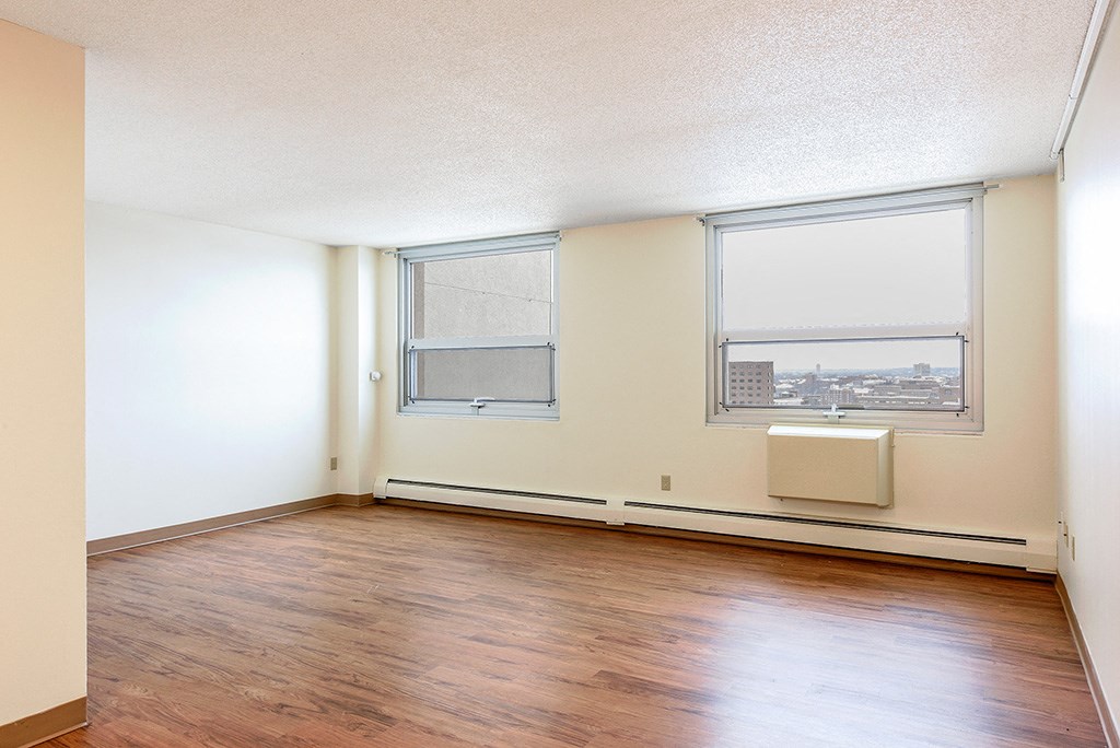 an empty room with wood flooring and two windows