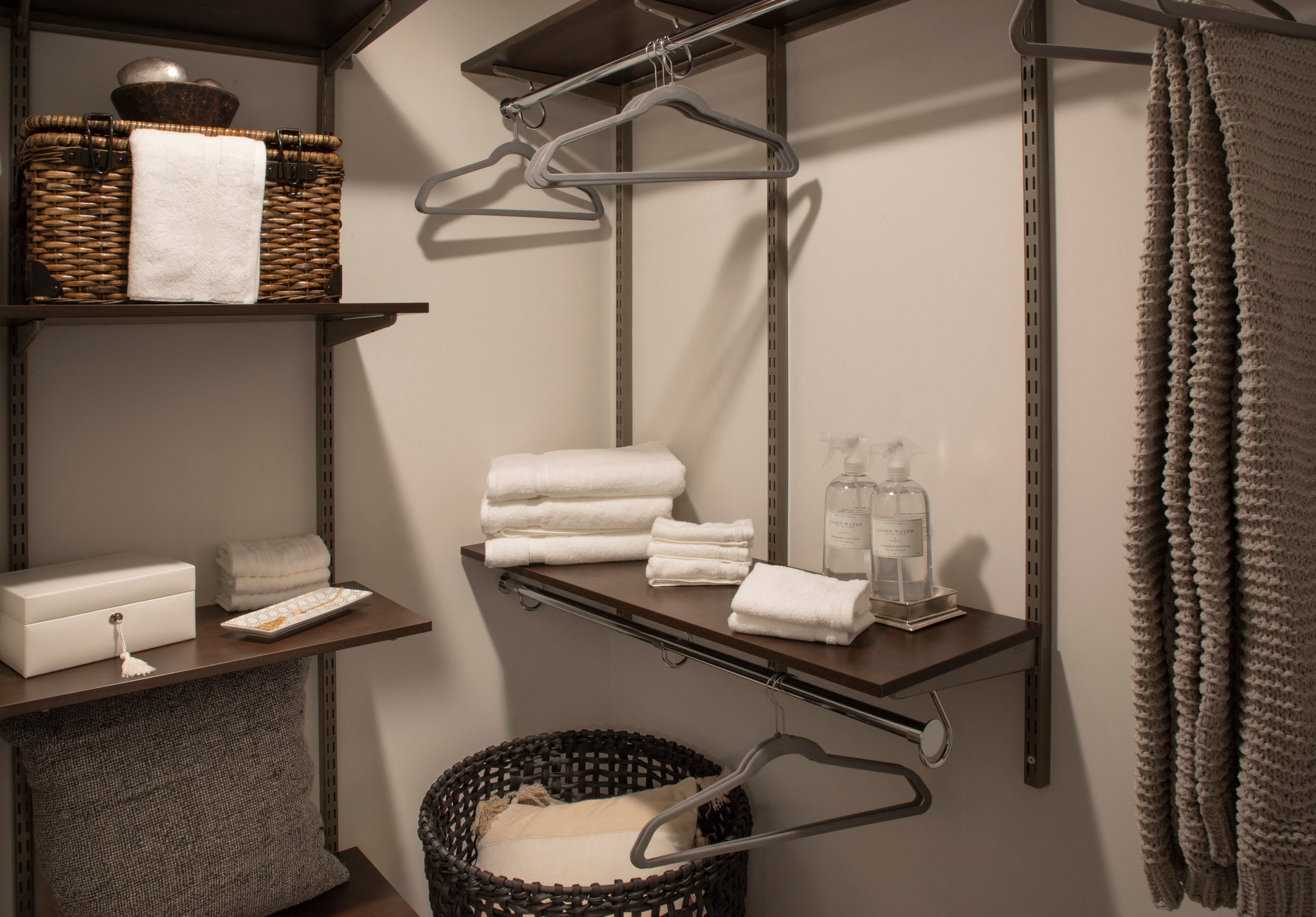 a small bathroom with a basket and shelves with towels and hangers