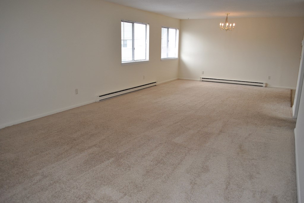 an empty living room with a carpeted floor and two windows