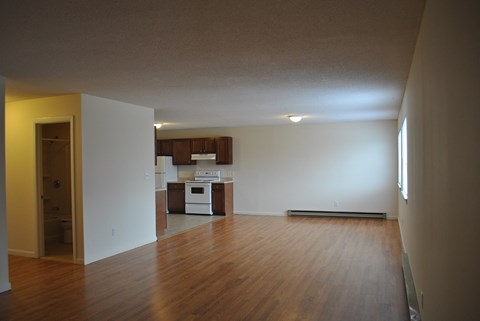 an empty living room with wood floors and a kitchen