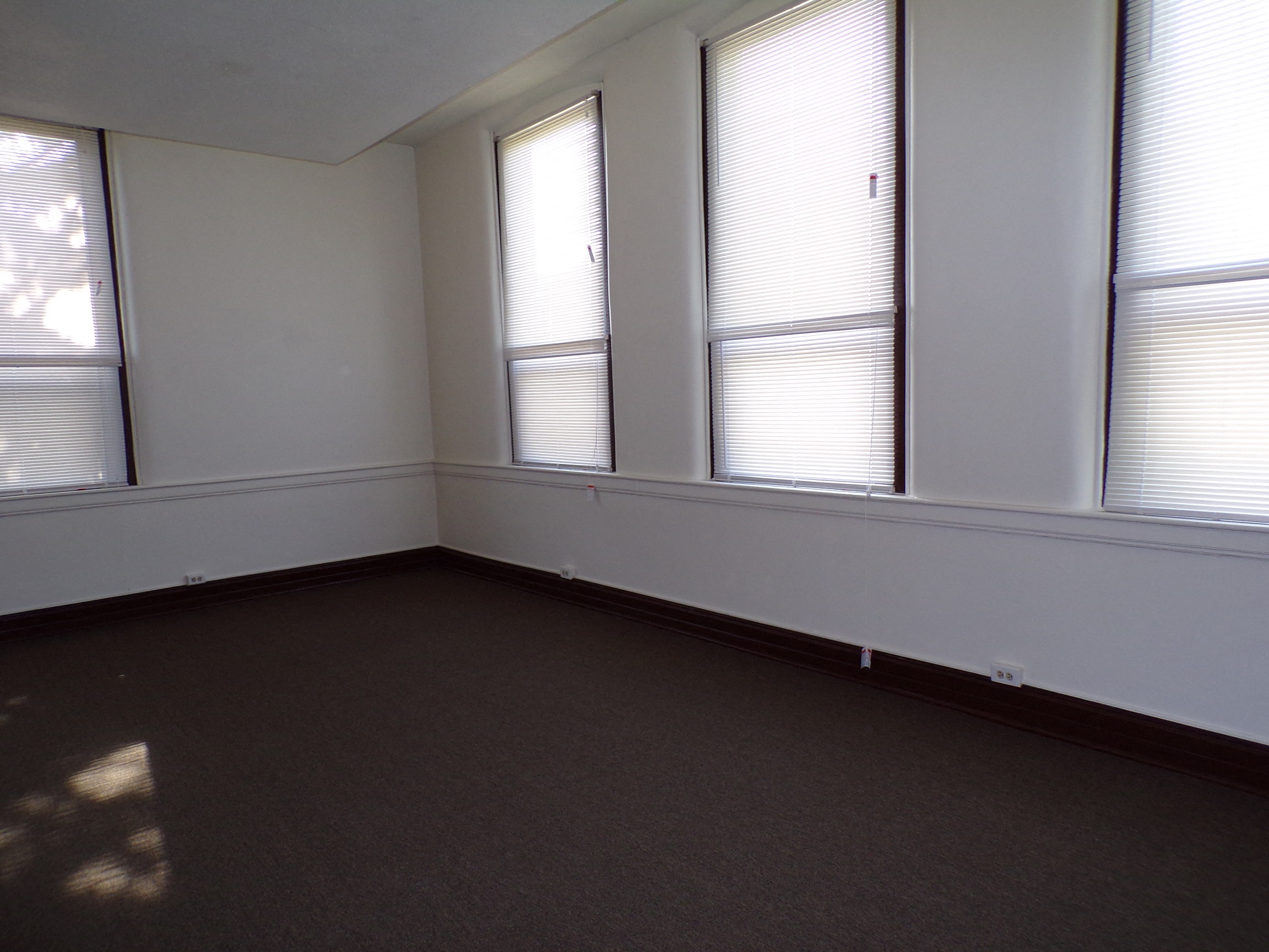 an empty room with three windows and a carpet