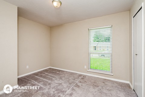 the spacious living room of this manufactured home has carpeted flooring and a window