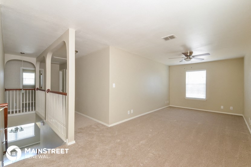 an empty living room with a ceiling fan and a staircase