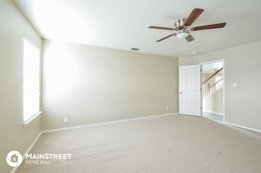 an empty living room with a ceiling fan and a white wall