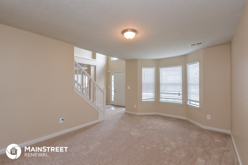 an empty living room with a staircase and large windows