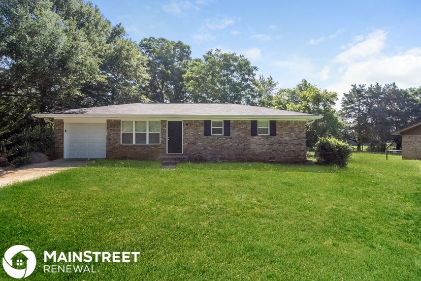 a small brick house with a grassy yard and trees