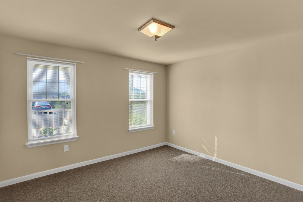 an empty living room with two windows and a carpet