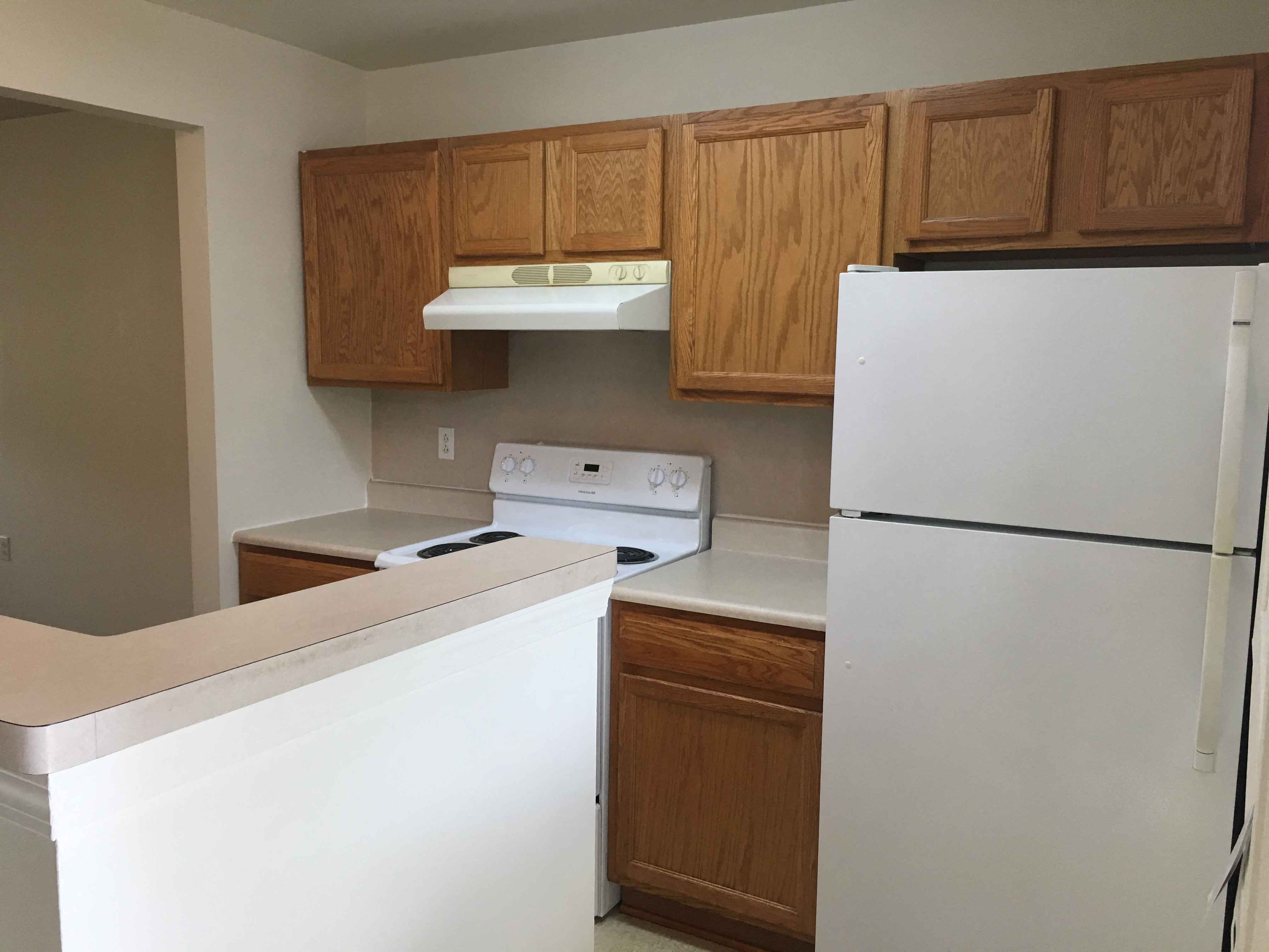an empty kitchen with white appliances and wooden cabinets