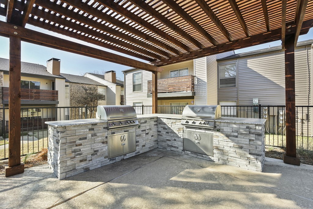a stone outdoor kitchen with stainless steel appliances and a pergola