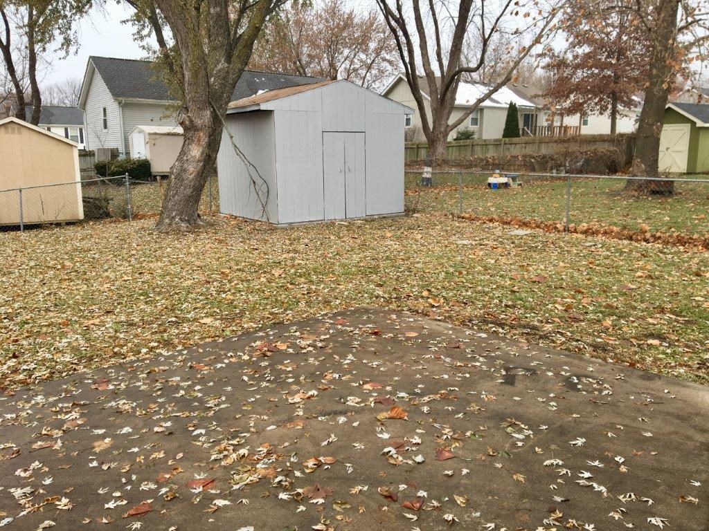 a shed in a yard with leaves on the ground