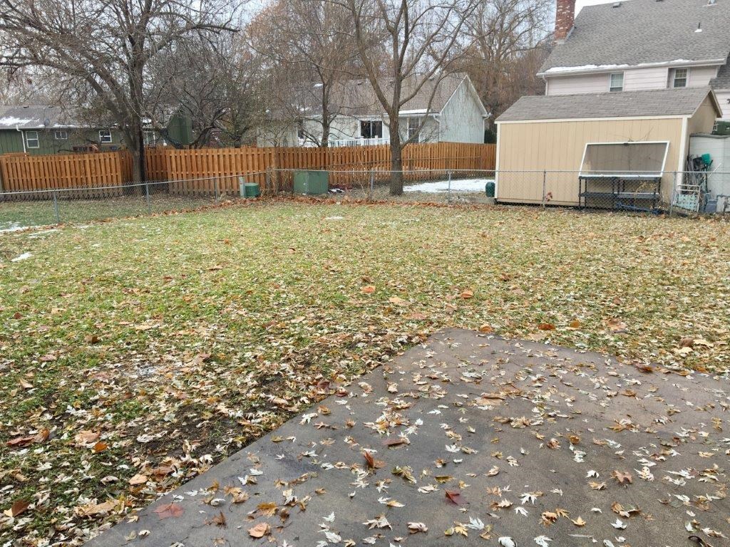 a yard with leaves on the grass and a fence