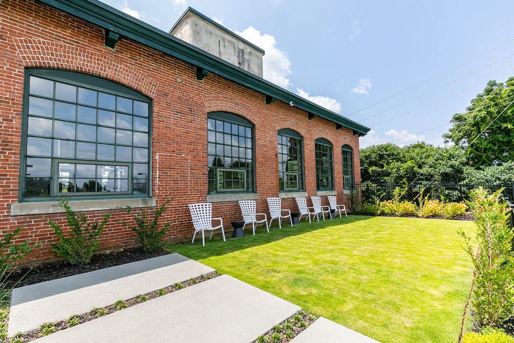 the outside of a brick building with chairs on the lawn
