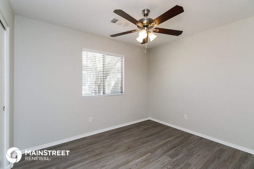 the spacious living room has a ceiling fan and wood flooring