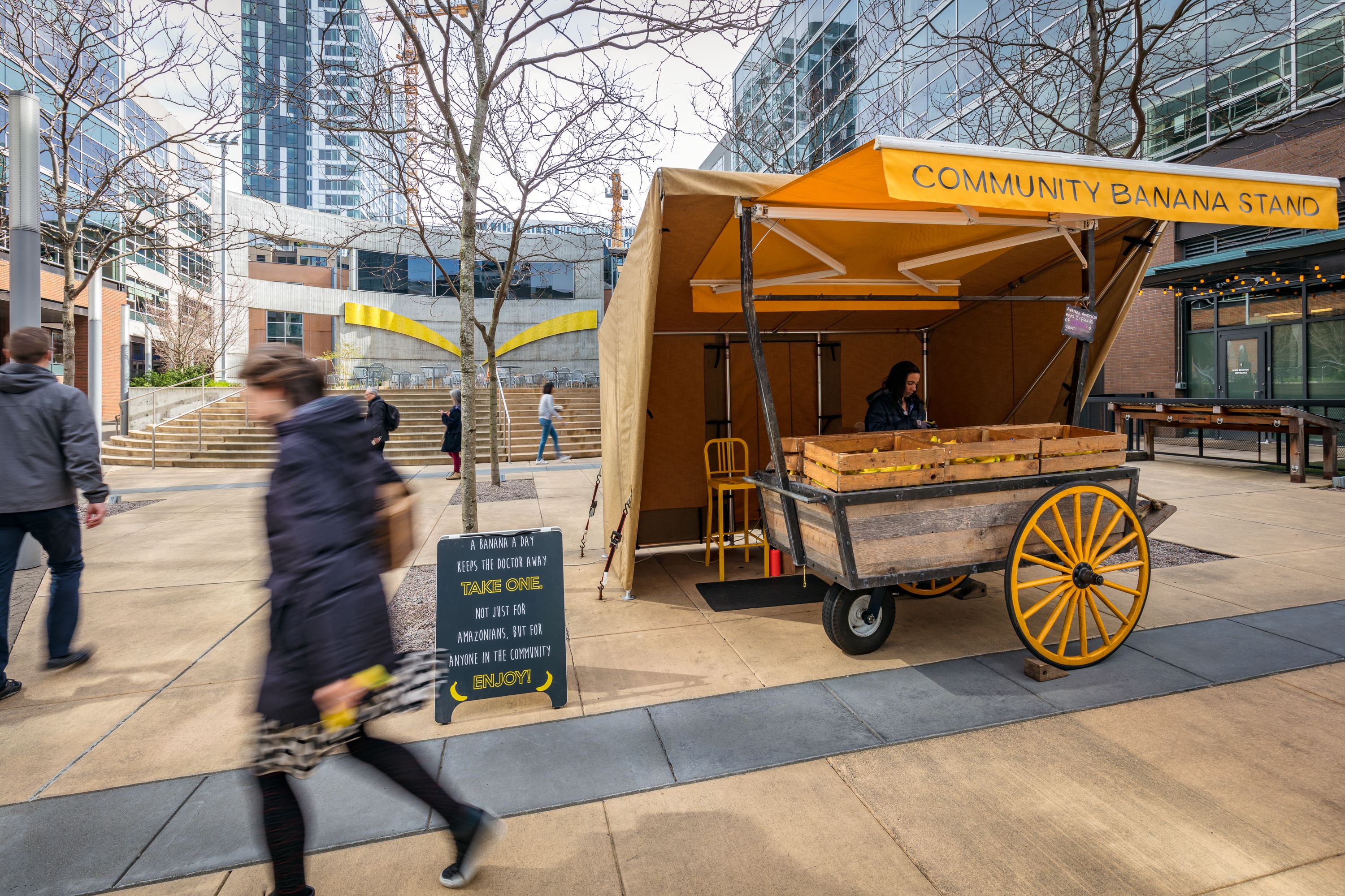 a woman walks past a yellow food cart on a sidewalk