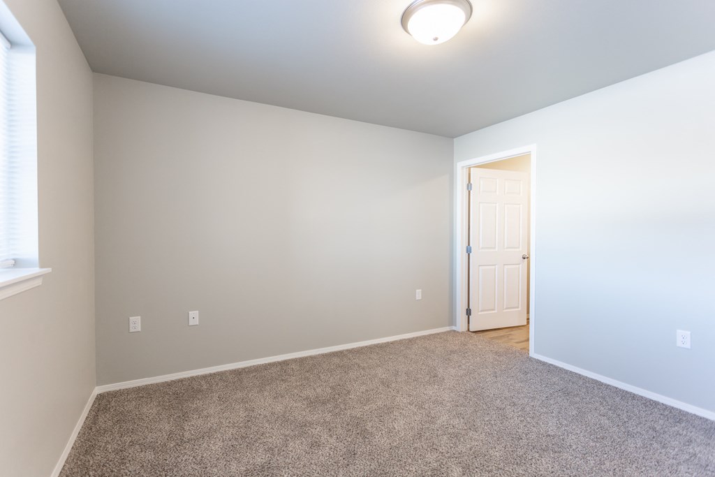 an empty living room with carpet and a door to a bedroom