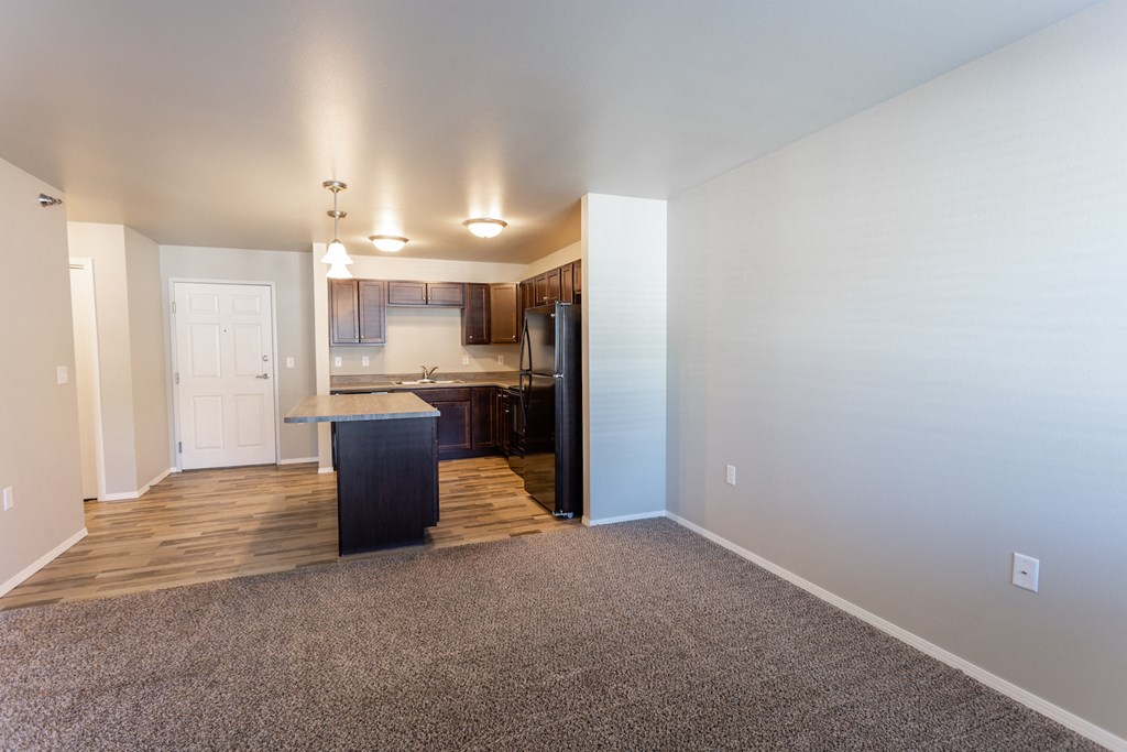 an empty living room and kitchen with wood flooring and white walls