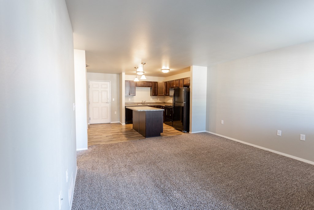 an empty living room with a kitchen in the background