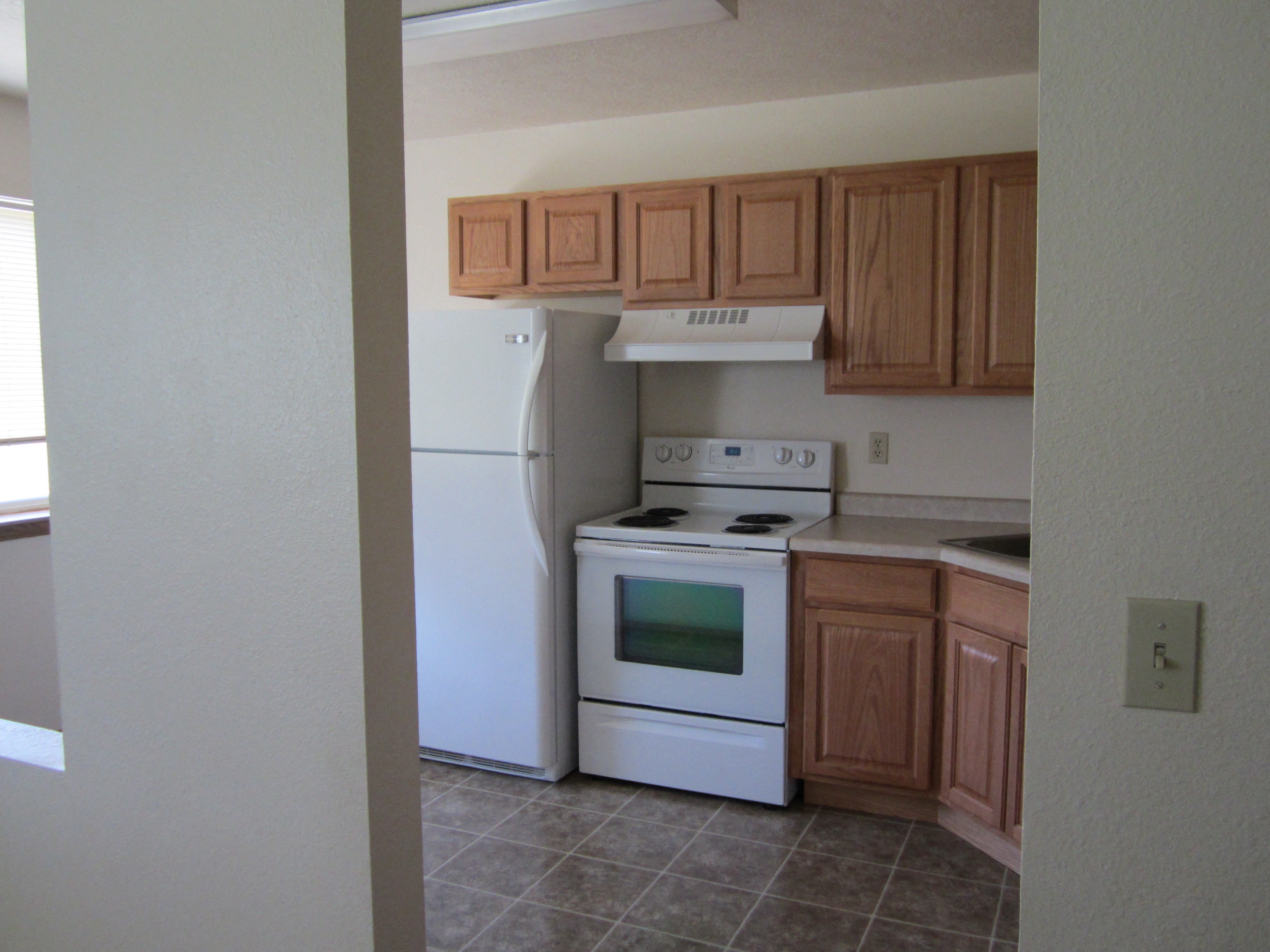 an empty kitchen with white appliances and wooden cabinets