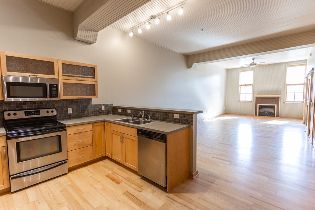 an empty kitchen and living room with wood flooring and stainless steel appliances