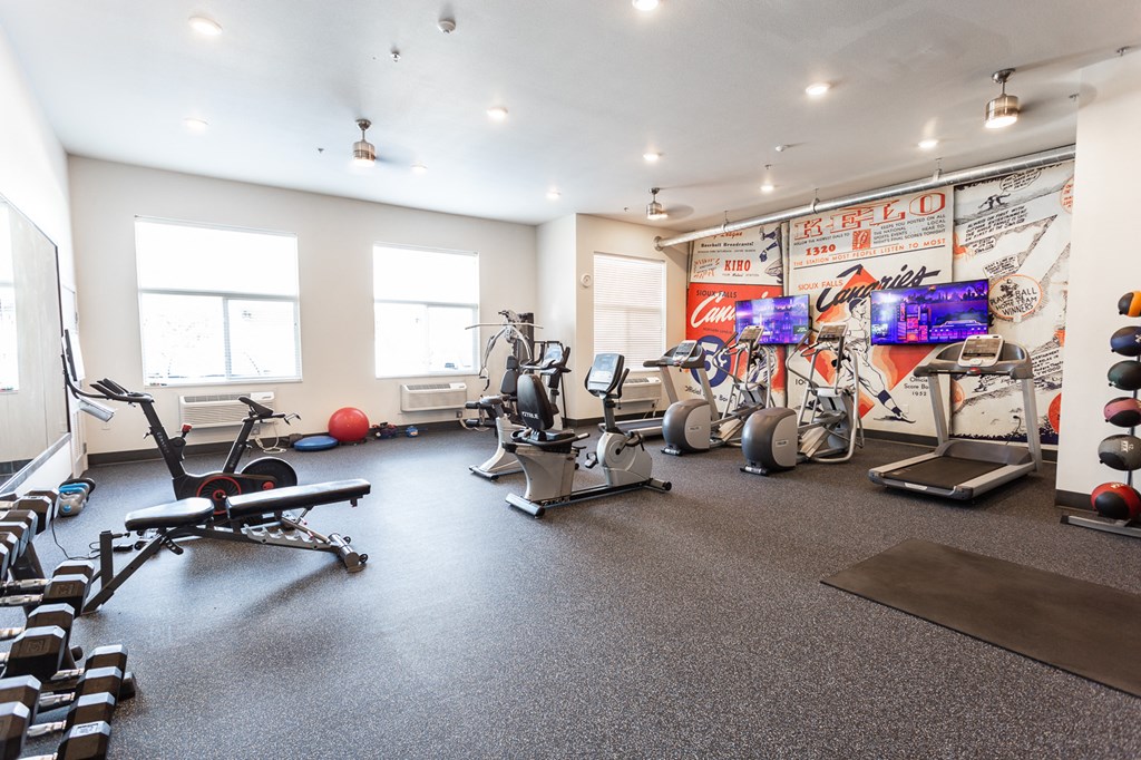 a gym with cardio machines and weights on the floor and a wall of graffiti