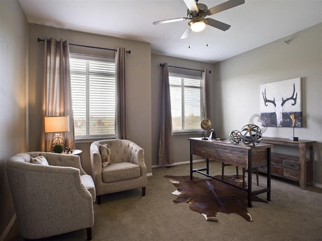 a living room with chairs and a desk and a ceiling fan