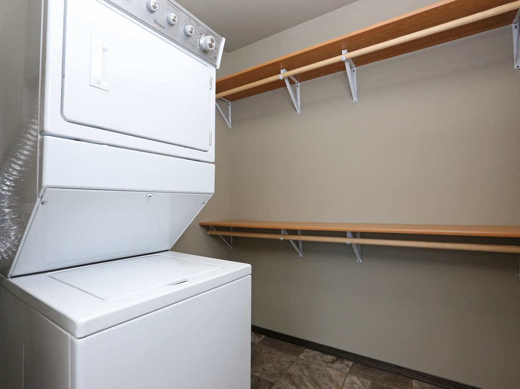 a laundry room with a washer and dryer and a shelf with hanging clothes