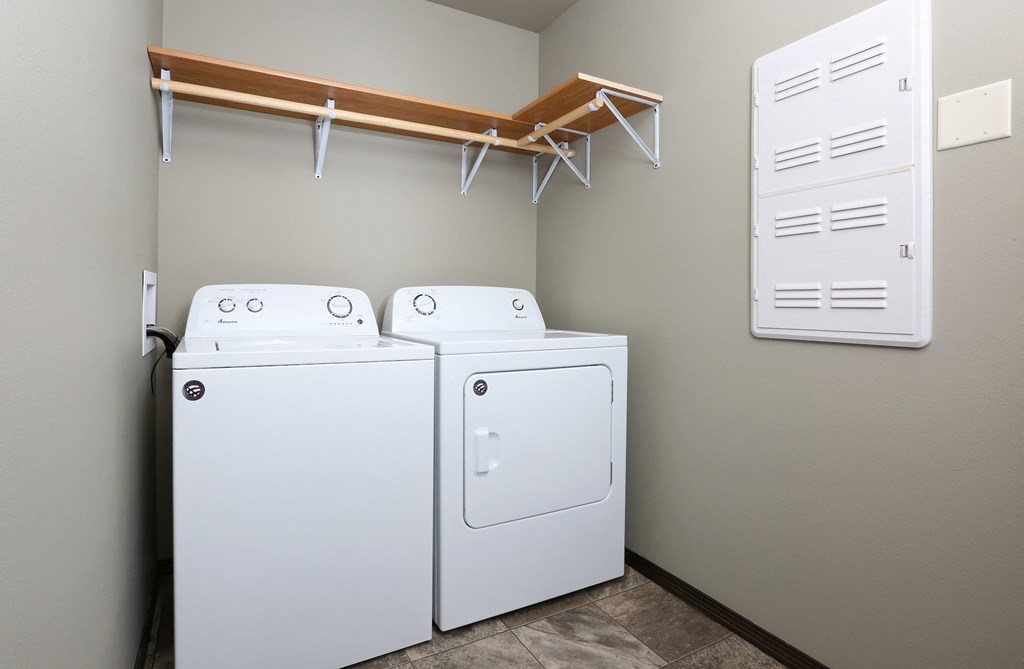 two washers and two dryers in a laundry room with a wall mounted rack