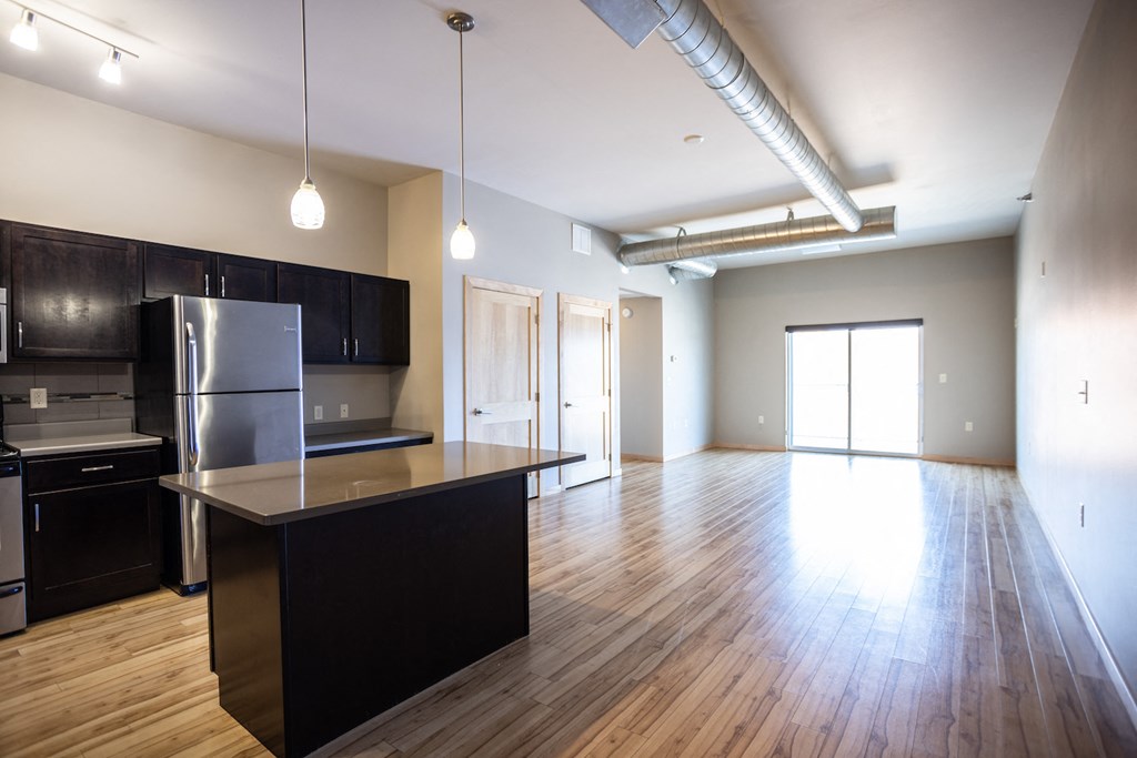 an empty kitchen and living room with wood flooring and a stainless steel refrigerator