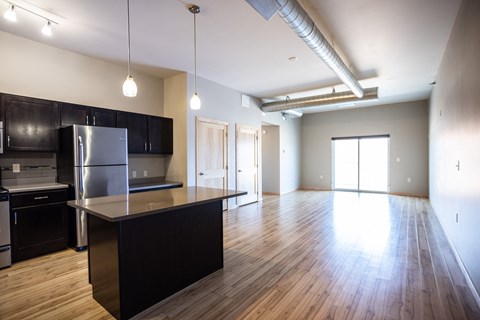 an empty kitchen and living room with wood flooring and a stainless steel refrigerator