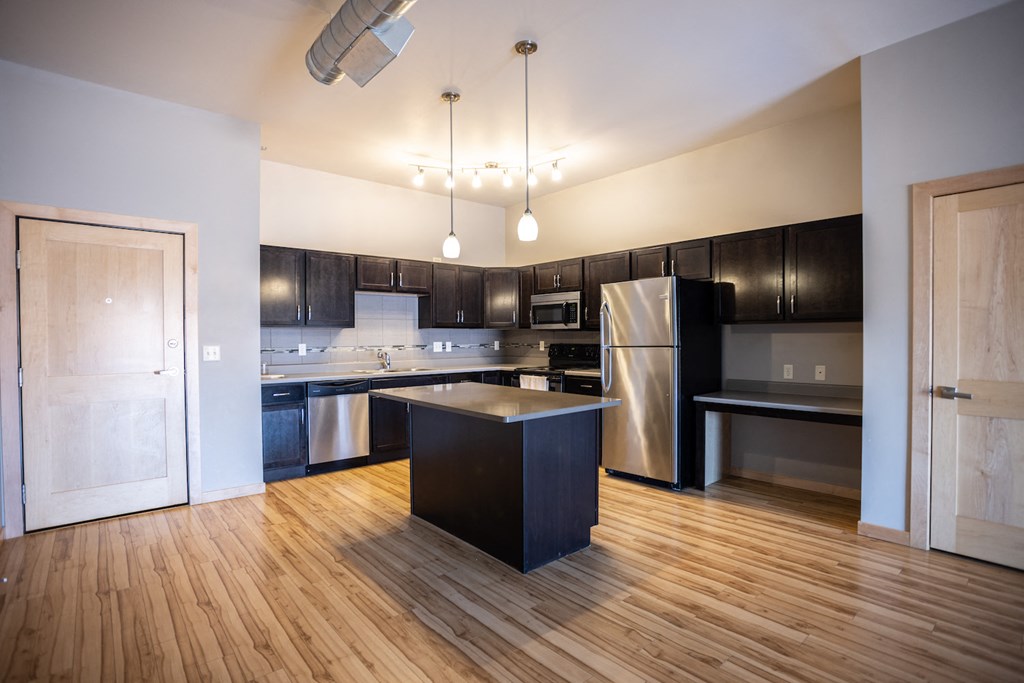 an empty kitchen with black and stainless steel appliances and wooden floors