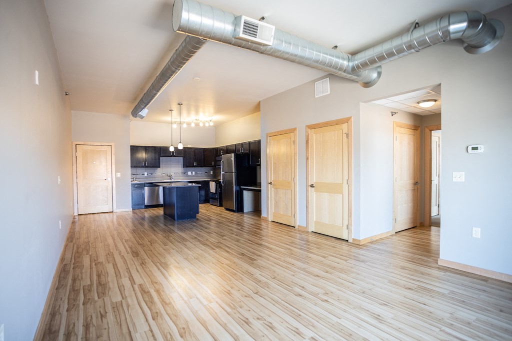 an empty living room with wood floors and a kitchen