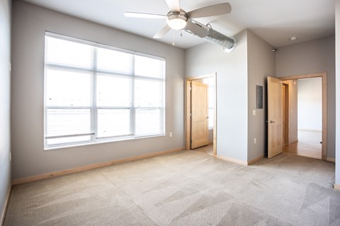 an empty living room with a large window and a ceiling fan